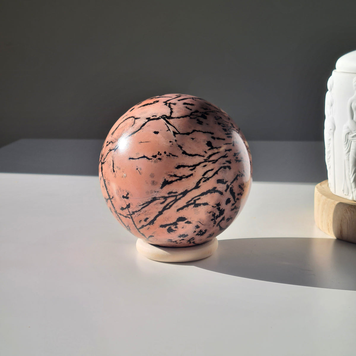 Picture jasper sphere on a pale stand, showing a peach face crossed by diagonal black markings.