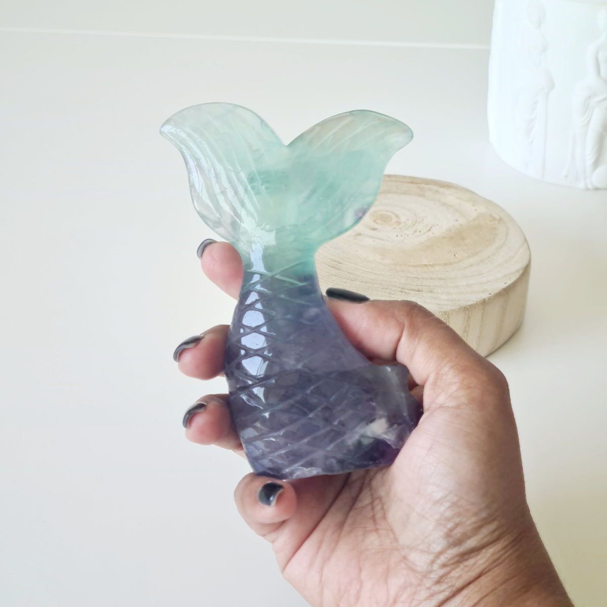 Hand holding a pale green and purple fluorite mermaid tail carving.