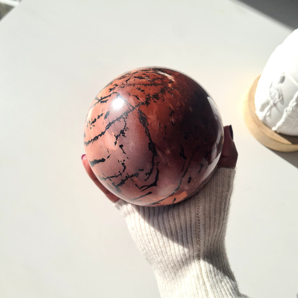 Hand-held picture jasper sphere showing rust-red patches and curved black lines.