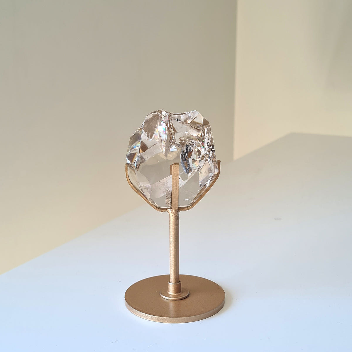 Irregular translucent smoky quartz crystal held in a gold-coloured stand with a round base.